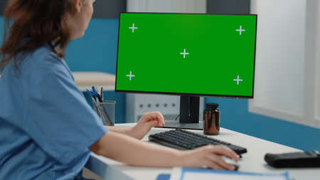 Close up of woman nurse looking at horizontal green screen on computer. Medical assistant using...