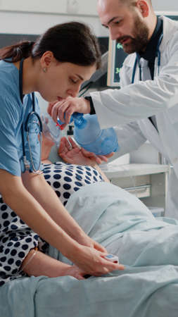 Old woman breathing heavily and asking for medical assistance while doctor and nurse helping with...