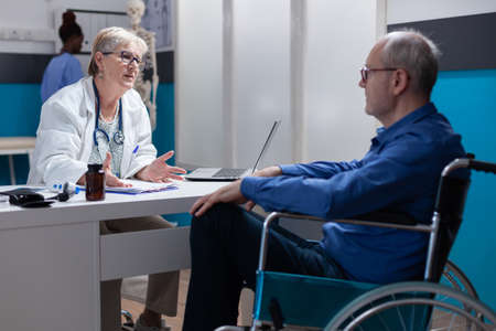 Physician talking to man with disability at annual checkup visit in medical cabinet. Medic having...