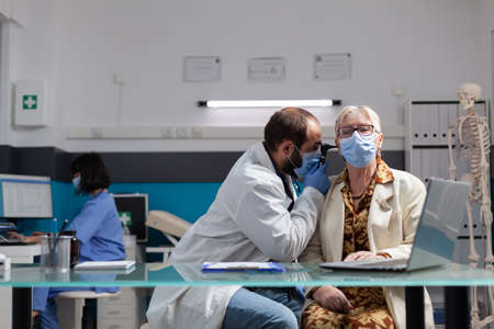 Health expert using otoscope to consult retired patient at medical appointment. Doctor doing ear...