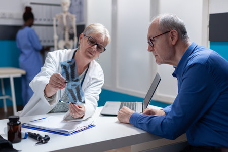 Woman doctor and man analyzing x ray scan exam results at checkup appointment in office. General practitioner explaining radiography diagnosis to patient with disease. Medical examinationの写真素材