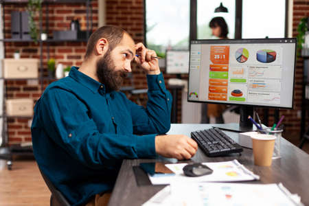 Focused pensive entrepreneur sitting at table thinking at project ideas working at marketing strategy planning business presentation. Concentrated businessman analyzing data charts in startup officeの写真素材
