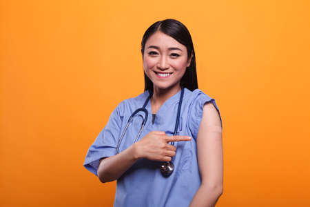 Smiling confident nurse promoting immunization through vaccination while wearing a band aid. Young confident positive caregiver encouraging people to immunise by getting anti-covid injection.の写真素材