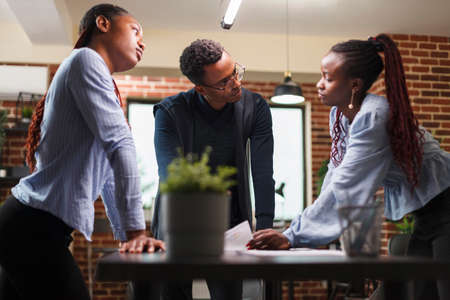 African american business company colleagues in meeting about startup project financial status. Marketing agency team members reviewing accounting documentation and revenue statistics data.の写真素材