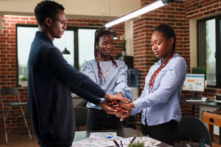 African american financial department team putting their hands together to celebrate business success. Marketing company employees celebrating successful startup project results and financial growth.の写真素材