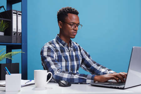 Serious firm project manager sitting at desk in modern office while using laptop to develop...