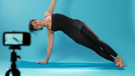 Yoga instructor filming stretching exercise on camera in studio, showing relaxing moves after...