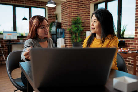 Entrepreneur women analyzing marketing graphs on laptop computer during business meeting in startup office. Businesswomen working at management project discussing company strategyの写真素材