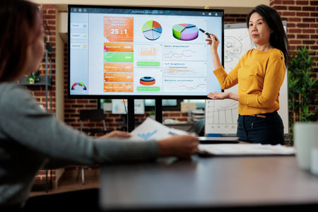 Asian businesswoman showing marketing graphs using monitor discussing company strategy with manager...
