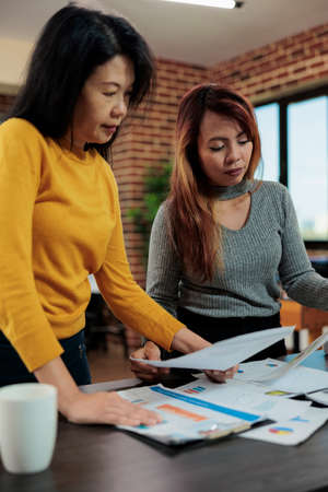 Executive managers looking at papers with management graphs analyzing statistics planning partnership project in startup office. Marketing team working at new strategu during business meetingの写真素材