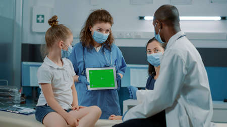 Tripod shot of assistant holding tablet with horizontal green screen to help physician. Nurse using...