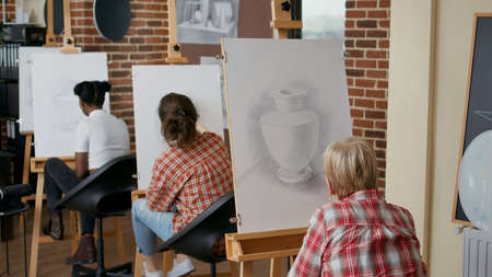 Elder student using pencil to draw on canvas in art class, attending lesson to develop artistic...