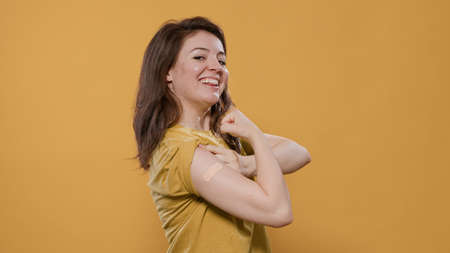 Portrait of smiling woman lifting sleeve and showing band aid after covid or flu vaccine for health...