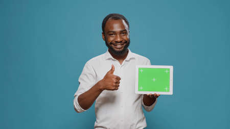 Happy man pointing at digital tablet with horizontal green screen in hand, showng isolated copy space with blank chroma key template and mockup background. Modern display technology.の写真素材