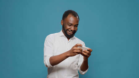Male gamer playing mobile video games on smartphone in studio, having fun with online gameplay as leisure activity. Excited joyful man enjoying cyberspace game on mobile phone.の写真素材
