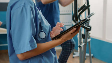 Health specialist in uniform using digital tablet to help senior patient with physical injury and...