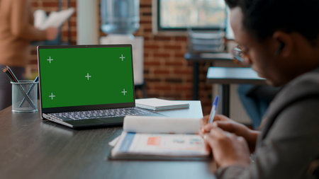 African american man looking at laptop with greenscreen in disability friendly office. Consultant taking notes and using chromakey copyspace with isolated mockup template and blank background.の写真素材