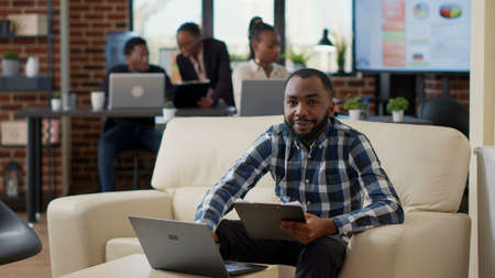 Portrait of male employee analyzing statistics on laptop and clipboard documents, using computer and...