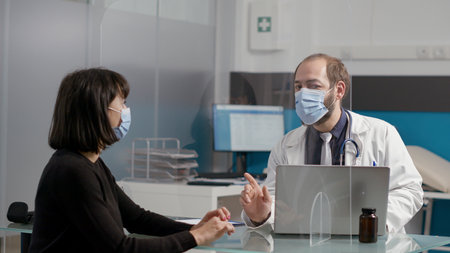 Patient and male doctor doing medical consultation in office during coronavirus pandemic. Young...