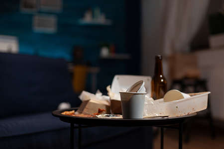 Empty messy living room with trash cans and leftovers rubbish on table, dirty space covered in...