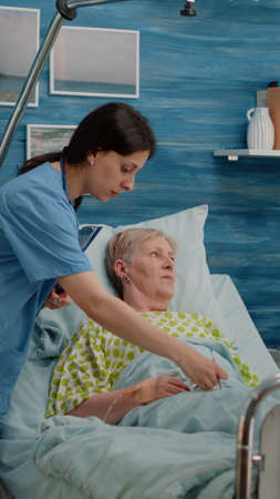 Medical team consulting patient with illness in bed at nursing home. Doctor doing healthcare checkup...