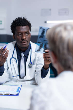 Radiology specialist reviewing senior woman radiography scan image while explaining recovery...