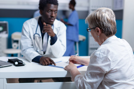 General practitioner explaining effects and side effects of prescribed painkillers to ill senior patient. Elderly woman signing discharge summaries and treatment clinic scheduleの写真素材