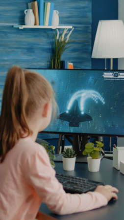 Young girl playing shoot video games on computer at desk. Child using action play for gaming and...
