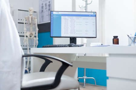 Computer with medical patient files on screen standing on table in empty doctors office during medical examination. Hospital office equipped with professional modern furniture. Health care supportの写真素材