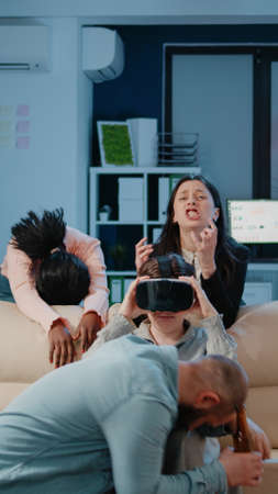 Colleagues enjoying drinks and video games on television after work. Woman playing game with...