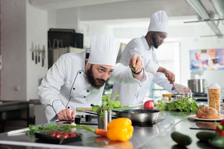 Head chef adding fresh chopped green herbs in pan while cooking gourmet dish in restaurant...