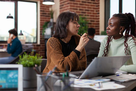 Multiracial group analyzing marketing statistics on laptop computer discussing company strategy...