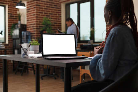 Mockup image of businesswoman sitting at desk in office with whitescreen display work laptop. Business company employee working on computer with chroma key and isolated template.の写真素材