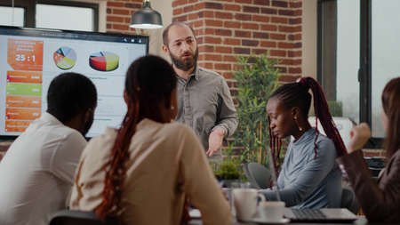 Business man presenting financial analysis on monitor, talking to colleagues at briefing meeting. Employee doing presentation in front of workmates, planning project development and growth.の写真素材