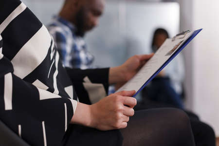 Close up of young adult woman hands holding CV resumes while sitting in lobby area of marketing...