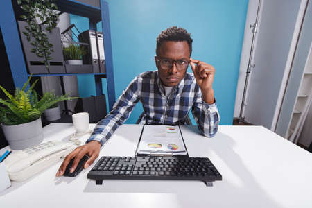 POV of unsure and sceptical young adult entrepreneur reviewing financial data using work computer. Doubtful african american businessman confused by wrongly declared accounting expenses.の写真素材