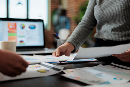 Close up of businesswomen hands holding business papers with management graphs on it working at company strategy in startup office. Marketing team brainstorming ideas for partnership projectの写真素材