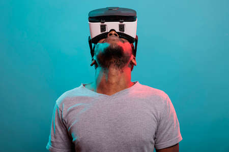 Male model looking up while he uses virtual reality glasses with interactive technology and 3d visual. Person using vr goggles with futuristic simulation to have fun experience in studio.の写真素材