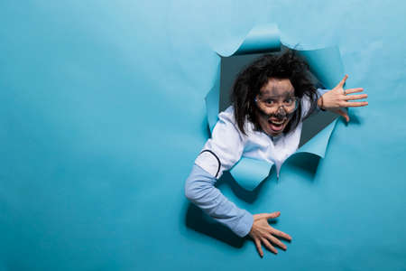 Foolish humorous scientist with comic expression on blue background. Young adult chemist with wacky...