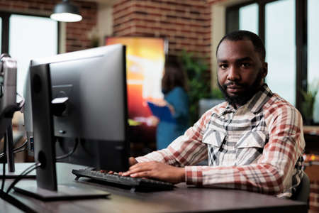 African american creative company employee sitting at desk in office workspace while looking at...