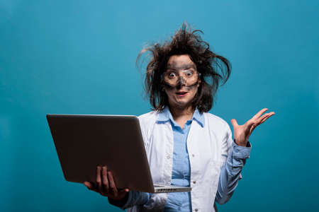 Lunatic chemist with messy hair and dirty face having laptop while gesticulating angrily after...