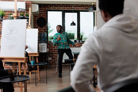 African american school teacher explaining sketch illustration to art students, teaching draw process having vase model for inspiration. Multiethnic group of creative people developing artistic skillsの写真素材