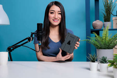 Asian content creator holding v mount power battery recording podcast for vlogging channel presenting videography production equipment. Social media influencer reviewing adapter portableの写真素材