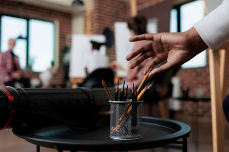 Close up of student hand taking graphic pencils in creativity studio. In background multi ethnic team drawing vase sketch on white canvas working at sketching technique. New years resolutionsの写真素材