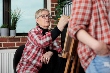Portrait of senior artist teacher sketching vase on canvas using graphic pencil during art class in...