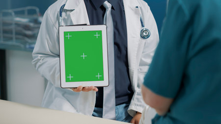 Physiotherapist vertically holding green screen on digital tablet with elder patient. Showing blank...