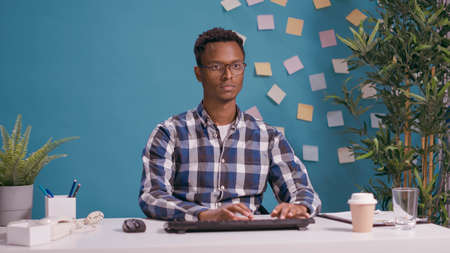 Portrait of african american man using computer at desk, looking at camera and working on business...
