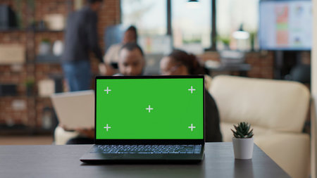Laptop with green screen display on desk in business office, team of people having isolated blank copy space with chroma key backgorund and mockup template. Modern technology. Close up.の写真素材