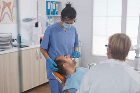 Dental woman nurse applying anesthesia with cotton swab before stomatological procedure in orthodontic office. Medical team discussing treatment against caries infection during dentistry examinationの写真素材