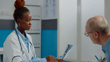 Close up of specialist looking at x ray scan with elder patient and talking about disease at medical...